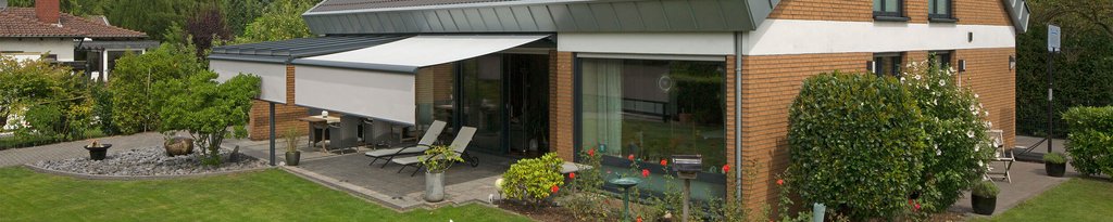 A modern house with a terrace featuring a retractable awning and green garden elements. A modern house with a terrace featuring a retractable awning and green garden elements.