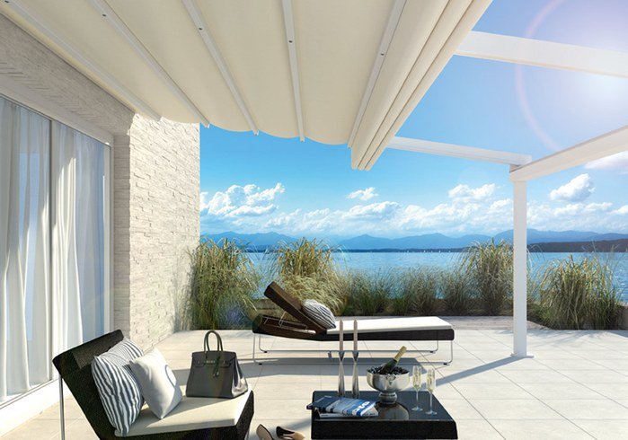 A spacious terrace with a sunshade, overlooking a serene lake and mountains in the background.
