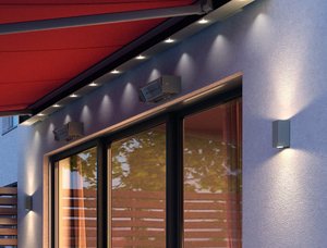 The image features a red awning with warm lighting on a textured wall, framing large windows.
