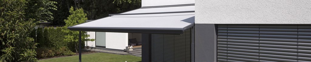 A grey awning extending from a building, with greenery in the background.