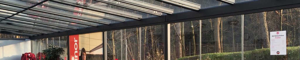 Glazed structure with a black frame and linear roof elements, surrounded by natural scenery.