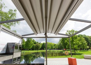 A view of a modern outdoor area with a large overhanging structure and a pond surrounded by greenery. 