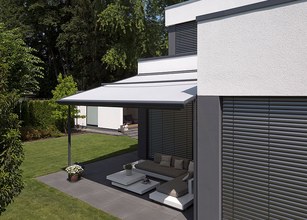 A modern house with a white awning, green lawn, and a terrace area featuring minimalist furniture. 