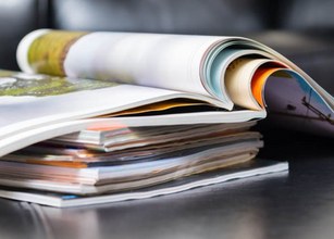 A stack of magazines with various colours and curled pages on a dark surface. 