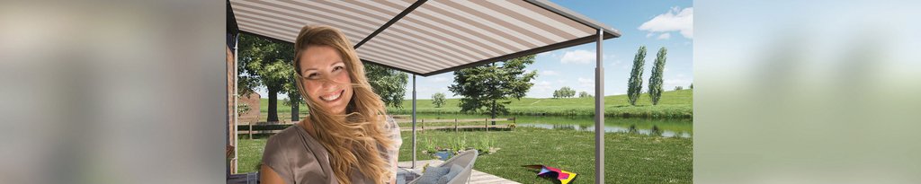 A smiling woman under a pergola with a striped awning, surrounded by greenery and a serene landscape.