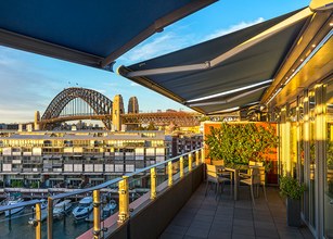 Balcony view with awnings, Sydney Harbour Bridge in the background and various structures by the water. 
