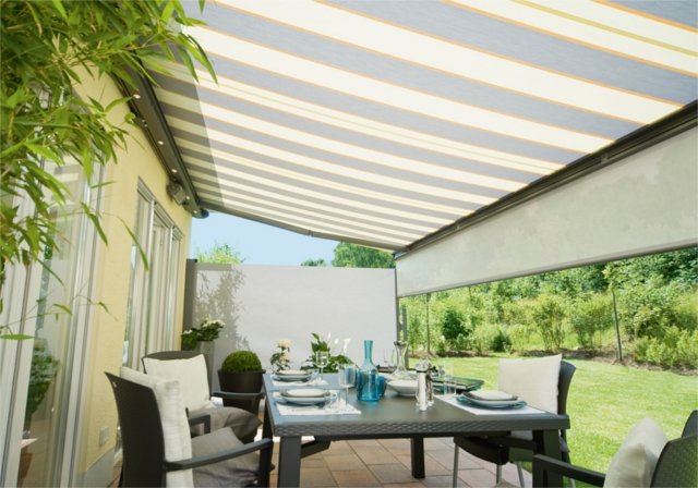 An outdoor dining area under a striped awning with a table set for a meal.