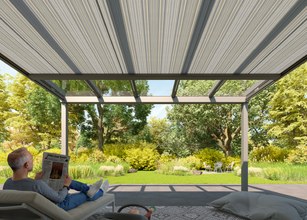A person sitting on a lounge chair reading a newspaper under a modern overhang with green garden views. 