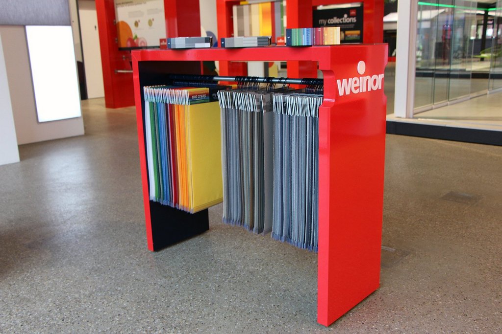 A red display stand holding various coloured samples, with grey, blue, yellow, and black hanging below.